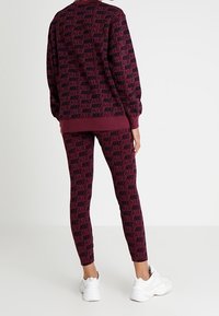 Burgundyröd träningsset med "NIKE AIR" mönster; sweatshirten har rund hals och långa ärmar, i kombination med åtsittande leggings och vita sneakers.