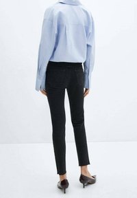 Jeans negros ajustados con bajos deshilachados, combinados con una camisa de botón oversized de color azul claro. Tela suave con detalles mínimos.