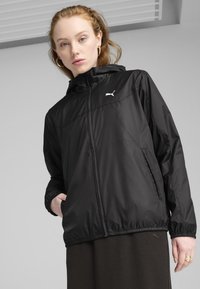 Veste légère noire à capuche avec une fermeture éclair sur le devant. Dotée de poignets et d'un ourlet élastiques, et d'un logo Puma blanc sur la poitrine gauche.