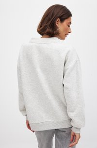Lichtgrijze sweatshirt van zachte stof, met een ontspannen pasvorm, verlaagde schouders en ribbelboordjes aan de mouwen en onderkant. Minimalistisch ontwerp.