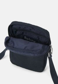 Námořnická crossbody taška se zipovým uzávěrem, která má podšívkovaný interiér a malou vnitřní kapsu. Vyrobena z odolné tkaniny s odnímatelným popruhem.