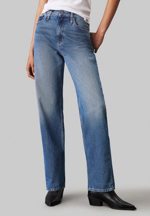 Jean en denim bleu clair avec une coupe droite, texture délavée et design à cinq poches, porté avec des bottines noires.