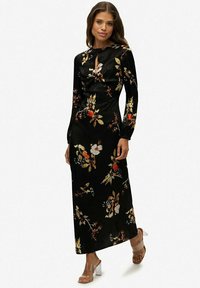 Czarna maksik sukienka z długimi rękawami, w kwiatowy wzór w kolorze czerwonym, żółtym i białym, z detalem w kształcie klucza przy dekolcie oraz gładką teksturą materiału.