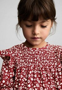 Punaviininen kukallinen mekko valkoisilla kuvioilla, kireä rintaosa ja röyhelöiset olkapäät. Kangas on tekstuuri, joka sopii lasten vaatteisiin.