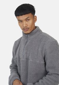 Szary polarowy sweter z wysokim kołnierzem, półzamkiem i teksturowanym, miękkim materiałem o luźnym kroju.