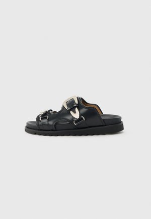 Μαύρο δερμάτινο σανδάλι με ανοιχτά δάχτυλα, δύο ρυθμιζόμενες ασημένιες αγκράφες και ανθεκτική μαύρη σόλα, εμφανιζόμενο από τη πλευρά σε γκρίζο φόντο.