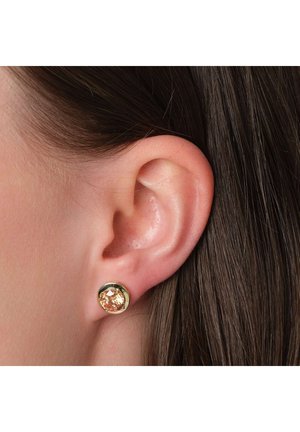 Goldene Ohrstecker mit einem runden, hellbernsteinfarbenen Edelstein, der in einer strukturierten Fassung gefasst ist, getragen am Ohr eines Modells mit dunklem, glattem Haar.