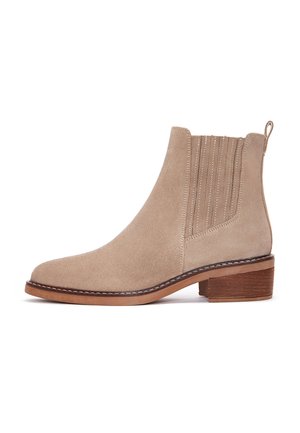 Stivale alla caviglia in suede beige con punta arrotondata, pannelli elastici laterali, dettagli di cucitura verticale e tacco in legno impilato.