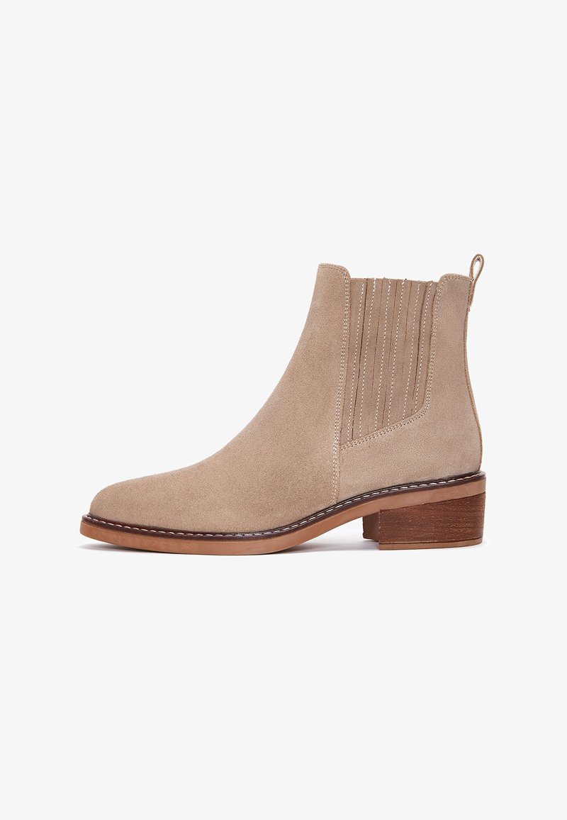 Stivale alla caviglia in suede beige con punta arrotondata, pannelli elastici laterali, dettagli di cucitura verticale e tacco in legno impilato.