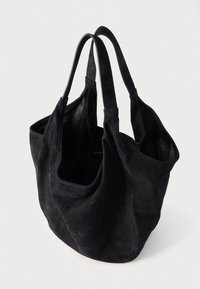 Sac fourre-tout en daim noir avec deux poignées, ouverture supérieure et deux poches latérales. Texture douce avec un design souple, sans ferrures ni motifs visibles.