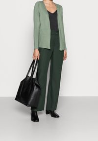 Světle zelený svetr, černý top, zelené kalhoty s vysokým pasem, černá kožená taška a kotníkov�é boty, s hladkými texturami a jednoduchým designem.