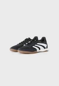 Black athletic shoes with white stripes, textured upper, and gum rubber outsole. Features lace-up design and green accents on the heel.