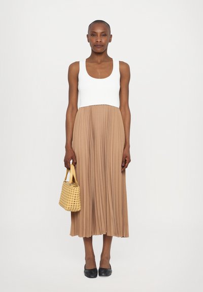 Top in bianco; gonna plissettata di lunghezza al ginocchio in beige; tiene una piccola borsa intrecciata gialla; ballerine nere; texture liscia.