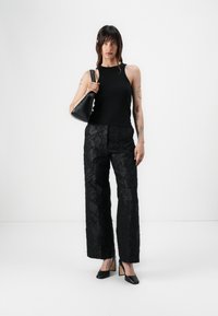 Black fitted tank top paired with black textured wide-leg pants featuring floral patterns. A small black handbag and pointed heels complete the look.
