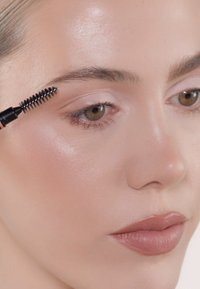 Augengelapplikator mit Spiralbürste, schwarzer Griff, Nahaufnahme von glatter Haut, hellrosa Lippenfarbe, natürlicher Make-up-Look.
