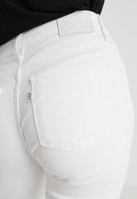 Primer plano del bolsillo trasero de unos jeans Levi's blancos con la etiqueta del logo de Levi's visible y una camiseta negra metida por dentro.