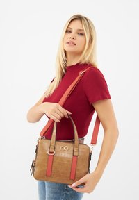 Sac à main marron avec motif crocodile et accents rouges, incluant des poignées. Équipé de doubles sangles, d'un logo doré et d'une forme rectangulaire.
