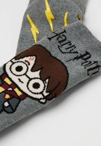 Graue Socken mit einem gestrickten Harry-Potter-Charakterdesign, gelben Blitzsymbolen und dem Text "Harry Potter" in Schwarz.