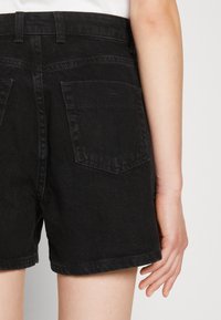 Pantalones cortos de mezclilla negra con una cinturilla alta, que cuentan con dos bolsillos traseros, detalles cosidos y un dobladillo limpio. Textura suave, desvanecimiento mínimo.