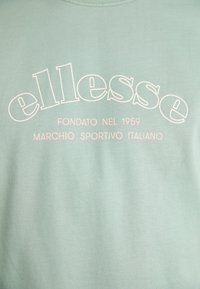Gaišzaļš T-krekls ar baltu un rozā tekstu: "ellesse," "FONDATO NEL 1959," un "MARCHIO SPORTIVO ITALIANO." Mīksta auduma, ikdienišķs dizains.