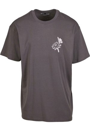 Siva bombažna majica s sproščenim krojem, z belim grafičnim dizajnom cveta in metulja na levem prsnem področju. Kratki rokavi in okrogla izrez.