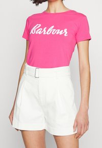 Růžové bavlněné tričko s bílým logem "Barbour", spárované s bílými vysokými šortkami v pase s páskem a sklady na přední části.