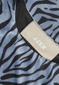Tessuto a rete blu con motivo zebra nero, con un'etichetta crema embossata con "JUXX" in bianco, e un bordo nero lungo il bordo.