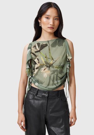 Green draped top with leaf pattern, sheer fabric, asymmetrical sleeves, and tie accents. Paired with high-waisted black leather pants.