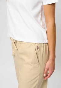 Hvid bomulds t-shirt med korte ærmer, parret med beige bukser med snøre, der har en lille broderet detalje på lommen.