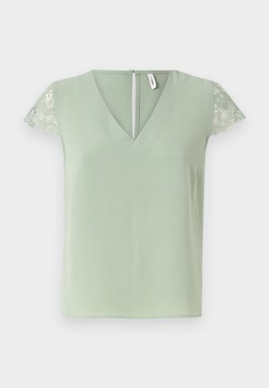 Lys grønne bluse med V-hals og korte blonder ærmer, med en lille åbning i ryggen og en glat stoftekstur.