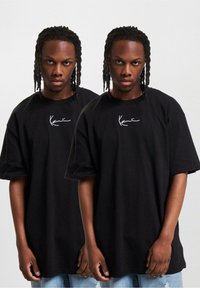 Black oversized t-shirt made of cotton with short sleeves and a round neckline; features a white cursive logo on the front.