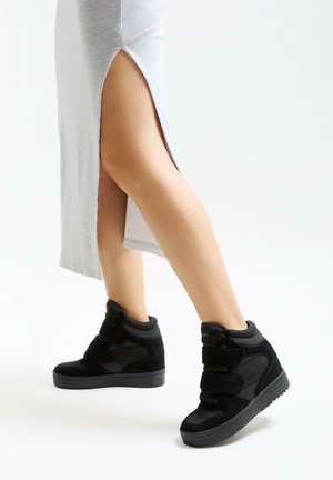 Baskets montantes noires avec un mélange de matériaux en daim et en mesh, dotées de trois bandes velcro et d'une semelle texturée.