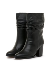 Botines de cuero negro con diseño holgado, punta afilada y tacón ancho. Textura suave con detalles mínimos.