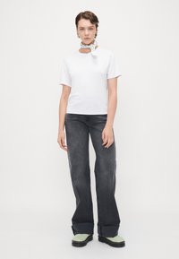 T-shirt bianca a maniche corte con scollatura rotonda, abbinata a jeans grigi scuri a campana e calzature verdi chiaro. Accessoriata con una sciarpa stampata.