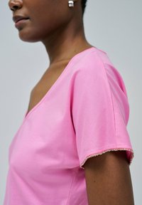 Top de manga corta rosa con escote en V, que presenta una textura suave y un dobladillo adornado con un brillo sutil.