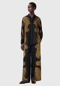 Camisa de seda preta e calças de perna larga adornadas com intrincados padrões dourados. A camisa apresenta um colarinho e mangas longas.