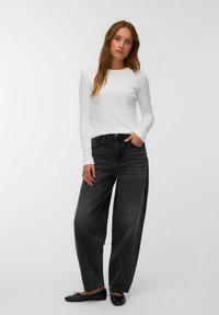 Bela srajca z dolgimi rokavi, črne široke jeans hlače, teksturirana tkanina, ravni črni čevlji, sproščen videz, nevtralna ozadja.