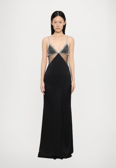 Robe noire avec un corsage transparent, un décolleté triangulaire orné et des bretelles fines. Présente une silhouette ajustée et un tissu lisse.