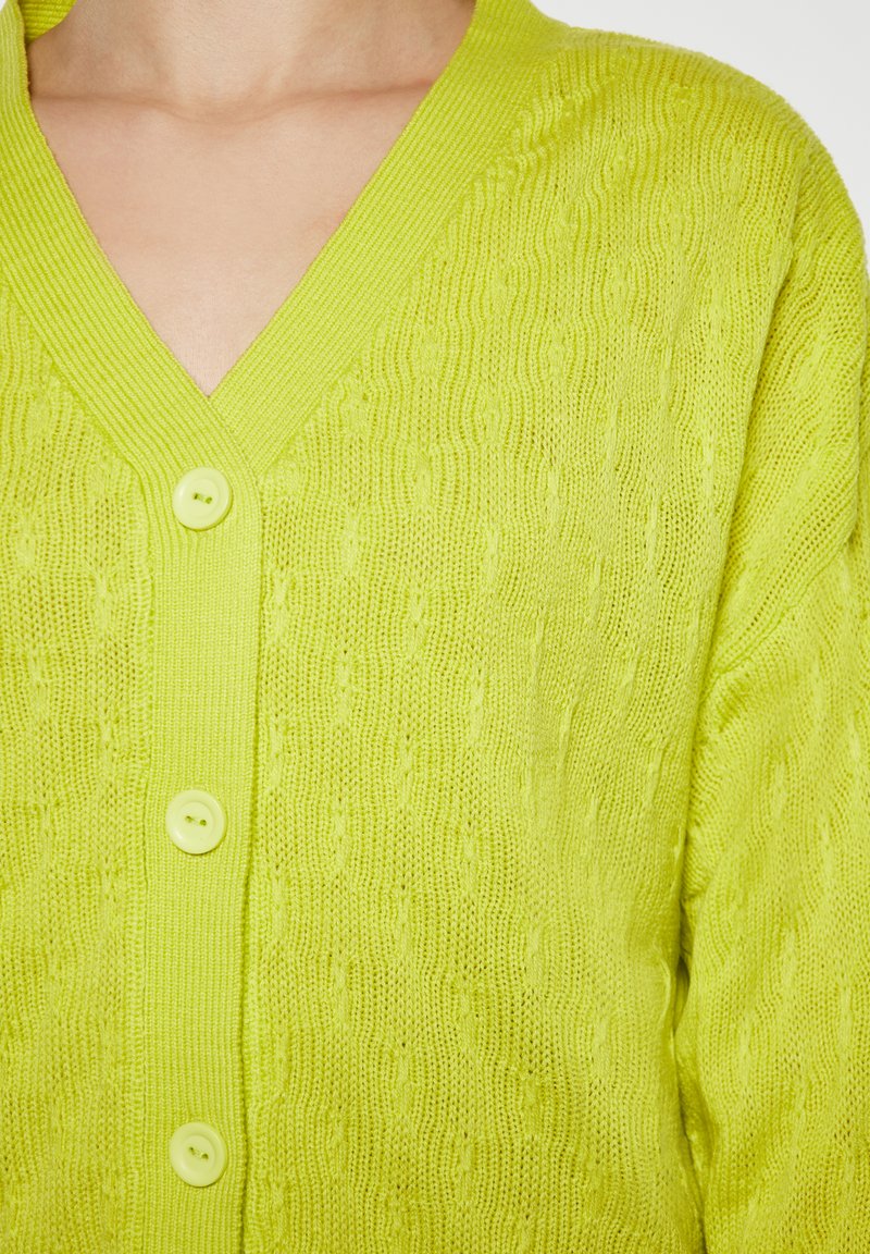 Cardigan lavorato a maglia verde lime con scollatura a V, caratterizzato da un motivo testurizzato e tre bottoni rotondi di colore verde chiaro sul davanti.