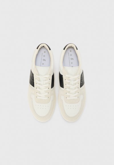 White and black leather sneakers with flat laces, rounded toe, perforated design on the toe box, and a contrasting black panel on the sides.
