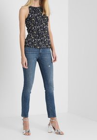Top senza maniche nero con motivo floreale, abbinato a jeans blu slim e sandali con tacco blocco argento. Design semplice e strutturato.