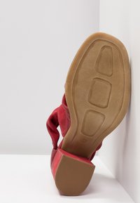 Chaussure à talon rouge inclinée vers le haut montrant une semelle beige texturée et un talon bloc empilé sur fond blanc.