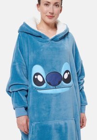 Felpa blu in peluche con cappuccio foderato di bianco, caratterizzata da un design con faccia di cartone animato con grandi occhi e un naso. Include una tasca frontale.