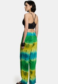 Spodnie tie-dye w luźnym kroju w kolorach zielonym, żółtym i niebieskim. Miękka tkanina; elastyczny pas; zestawione z czarnym, ramiączkowym topem.