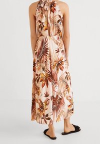 Robe maxi en tissu léger, dotée d'un col halter et d'un imprimé tropical vibrant avec des feuilles dans des tons de vert, marron et des touches d'orange.