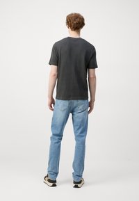 Tricou scurt, de culoare gri închis, cu o croială lejeră, asortat cu blugi drepti de culoare albastru deschis și sneakersi negri cu bej.