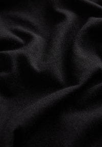 Gros plan sur un tissu noir doux avec une texture tricotée visible et des plis doux créant des ombres et de la profondeur.