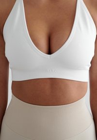 Witte crop top met een diepe V-hals en een geribbeld band. Gecombineerd met hoog getailleerde beige leggings. Gladde stoftextuur.