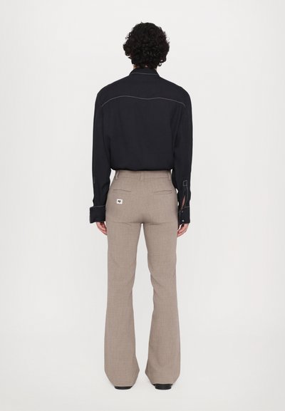 Men's outfit featuring a black button-up shirt with white stitching and beige flared pants with back pockets. Smooth, tailored fabric.