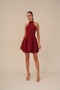 Robe rouge à col halter avec un corsage ajusté et une jupe évasée en couches. Fabriquée à partir d'un tissu texturé. Associée à des sandales à talons transparents.
